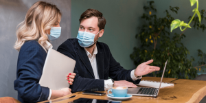 Businessman and woman in face masks seated at a table, engaged in a discussion or meeting.
